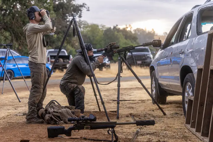 Kneeling tripod gun at dusk, spotter on binos