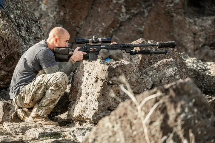 Crouched behind a suppressed rifle on rock