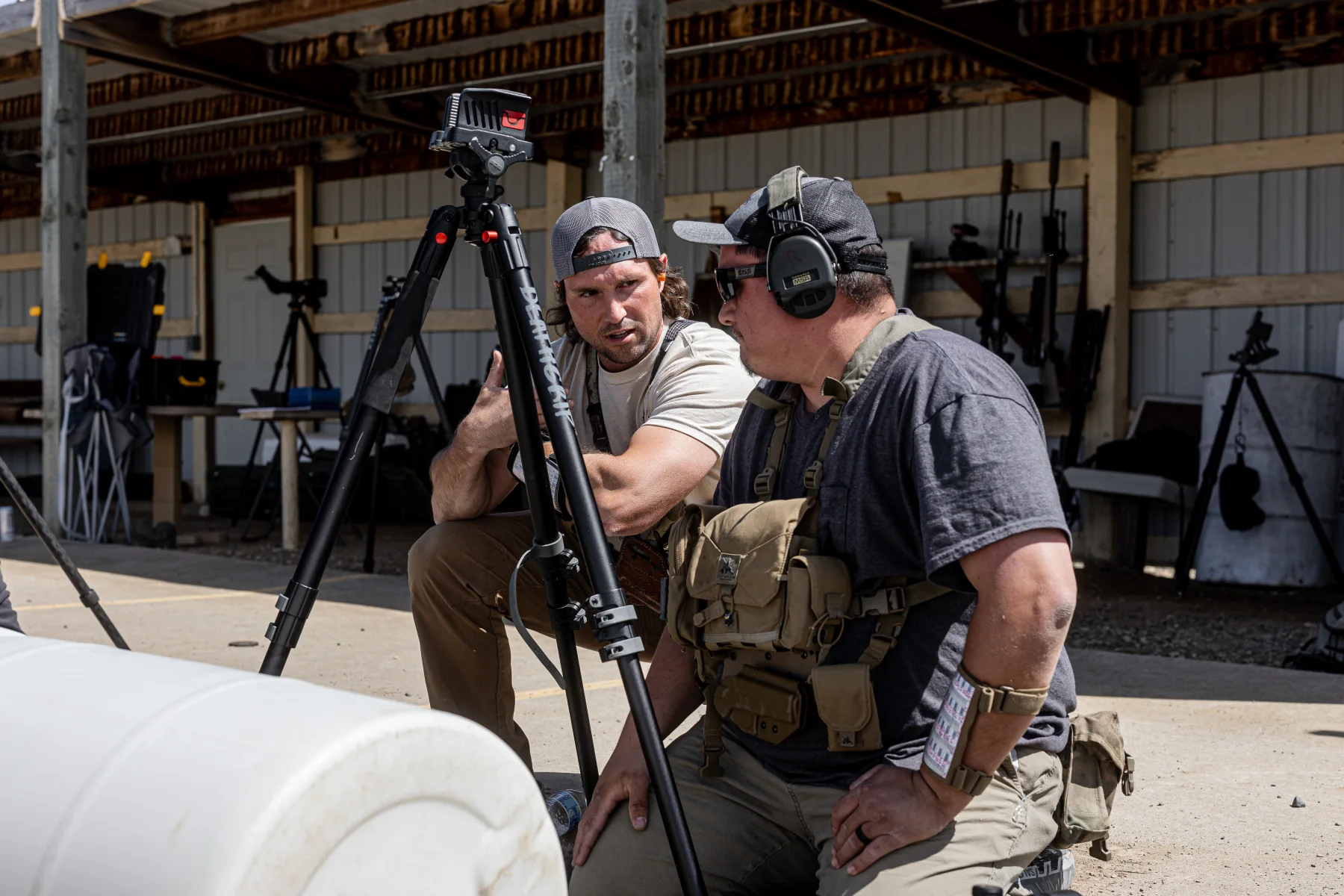 An instructor coaching a shooter beside a tripod-mounted optic