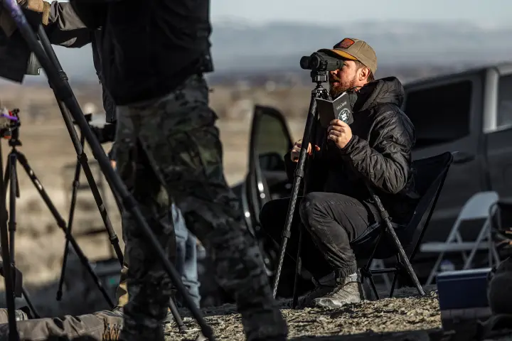 Seated behind a spotting scope, data book in hand