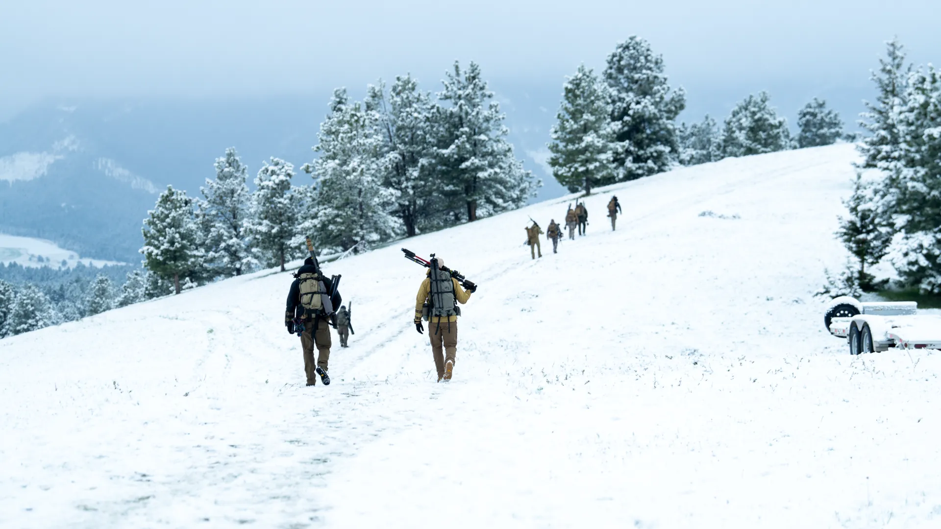 Shooters hiking a snowy ridgeline with rifles and packs on the way to a stage.