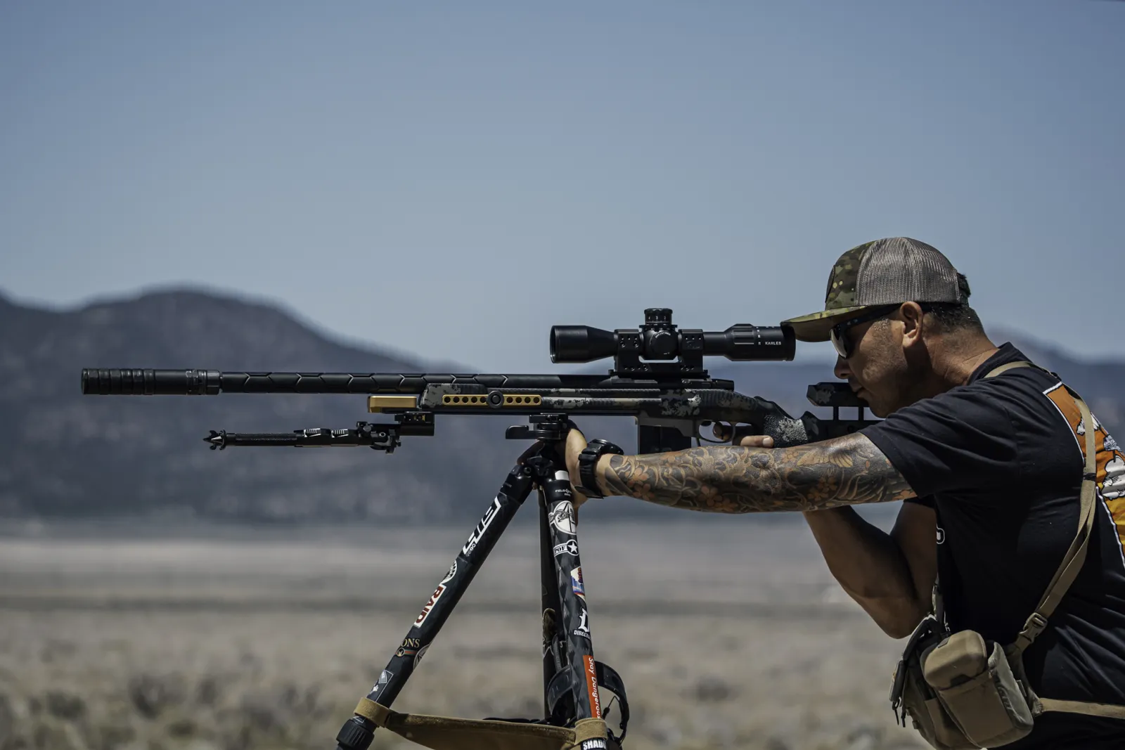 Beau Mattioda shooting a suppressed precision rifle from a tripod at The Invite in Utah, mountains behind him