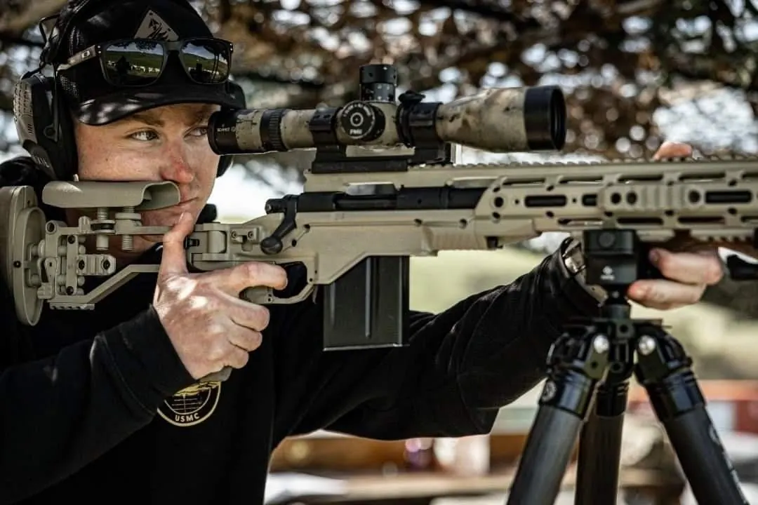 Caleb Neff aiming a precision rifle from a tripod, wearing ear protection