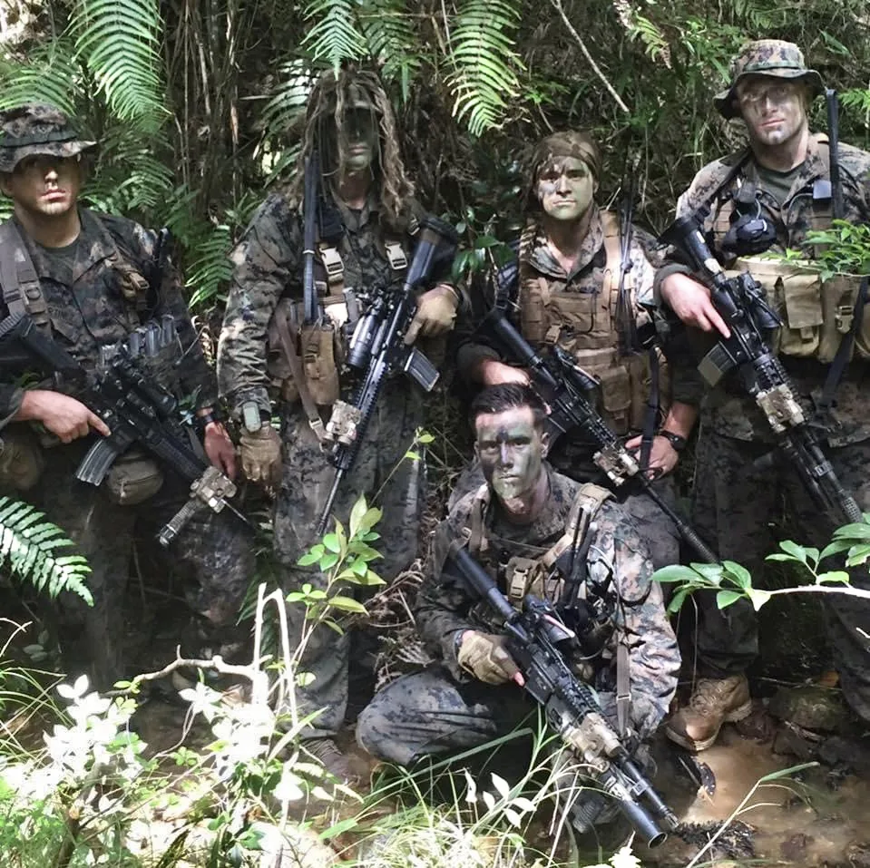 A Marine reconnaissance team in face paint and ghillie veils in dense jungle