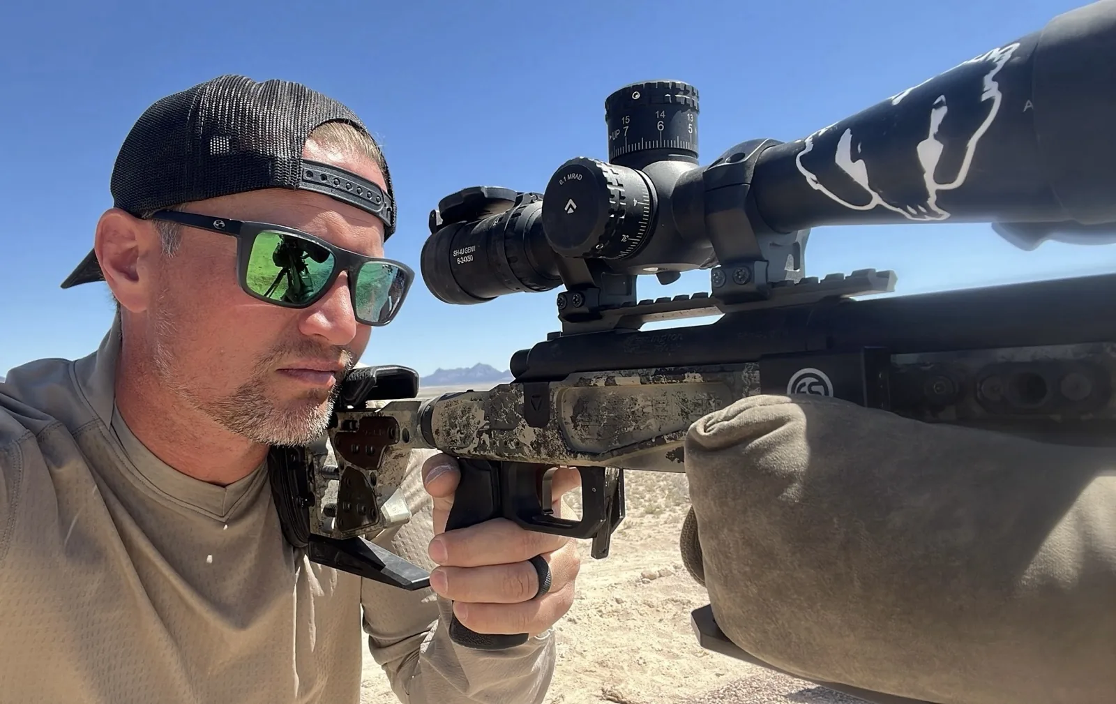 Close-up of Eric Avvisato behind his custom Remington precision rifle with an Arken scope in the desert