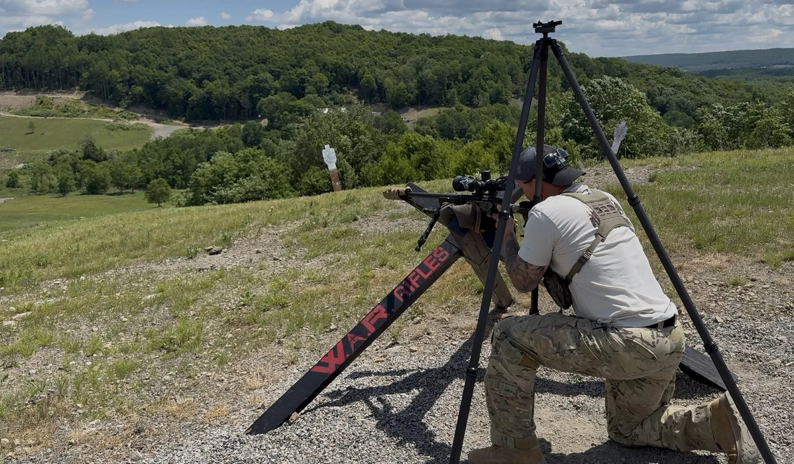 Eric Avvisato shooting a precision rifle off a tripod on a hillside firing line