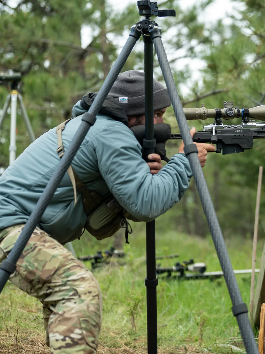 Eric D'Oro leaning into his rifle on a tripod against a wooden post barricade at an NRL Hunter match