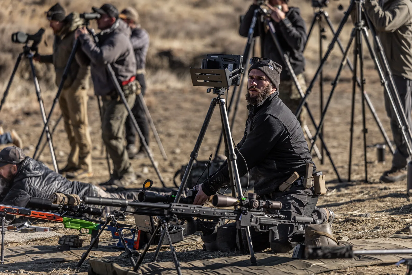Eric D'Oro setting up a trigger-cam demonstration on the firing line at The Invite, a row of shooters behind him