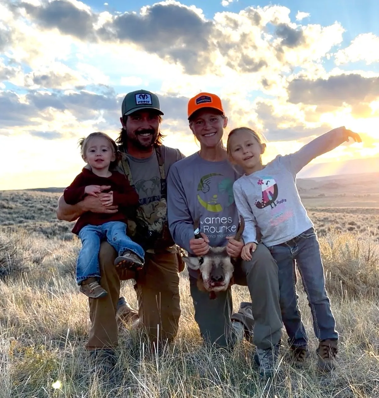 Ian Miner kneeling with his wife and two of his kids at sunset after a pronghorn hunt