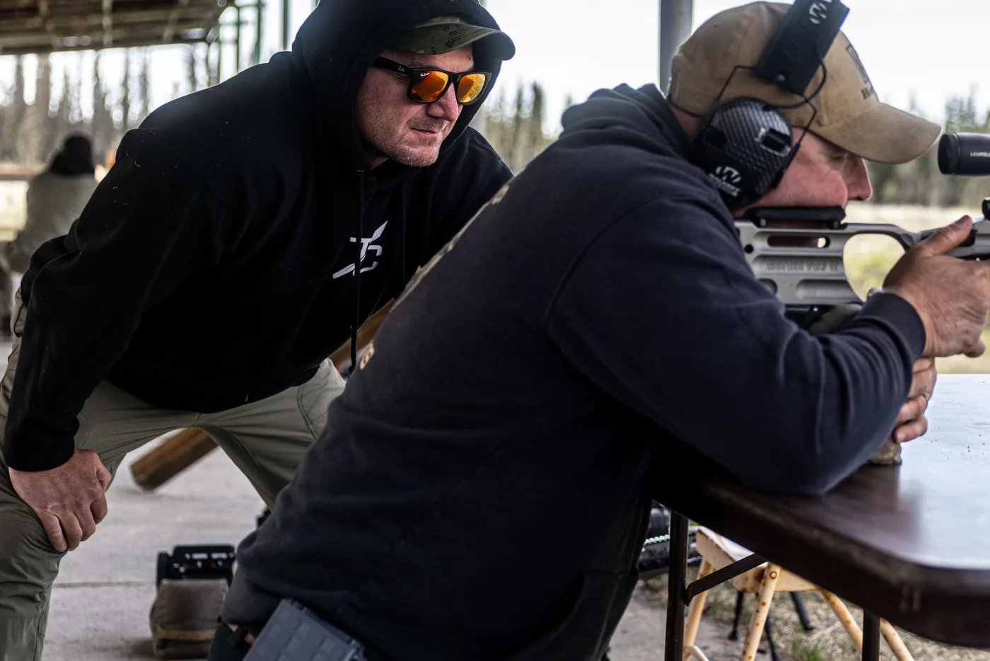 Matt Solowynsky in shooting glasses watching closely over a student's shoulder as they shoot off a bench