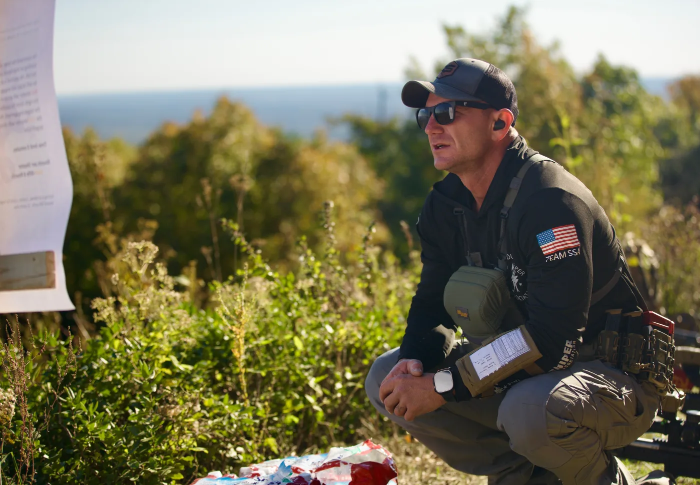 Matt Solowynsky kneeling at a stage board, reading the course of fire at a sniper match