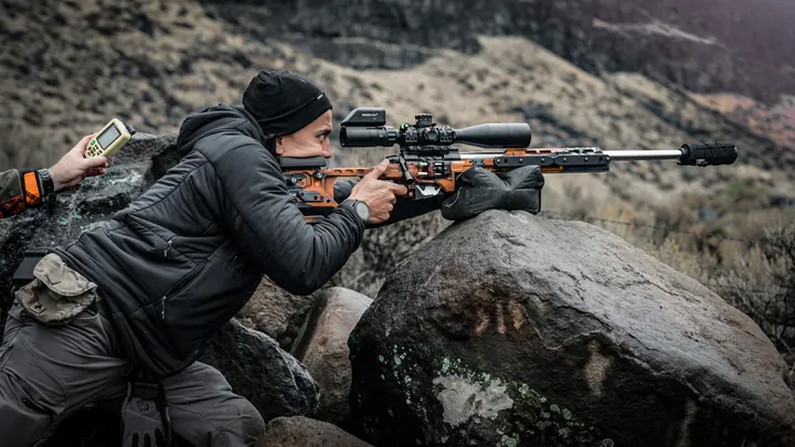 Phil Velayo leaning into a precision rifle rested on a bag on top of a boulder